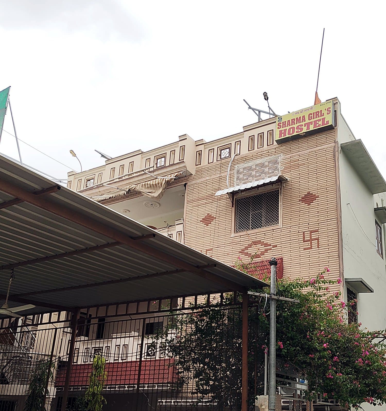 Front exterior of Sharma Girls Hostel showing the hostel signboard, entrance gate and building facade