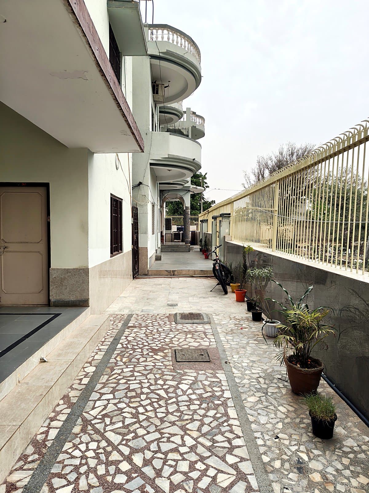 Paved side walkway along the hostel building with potted plants and boundary fence